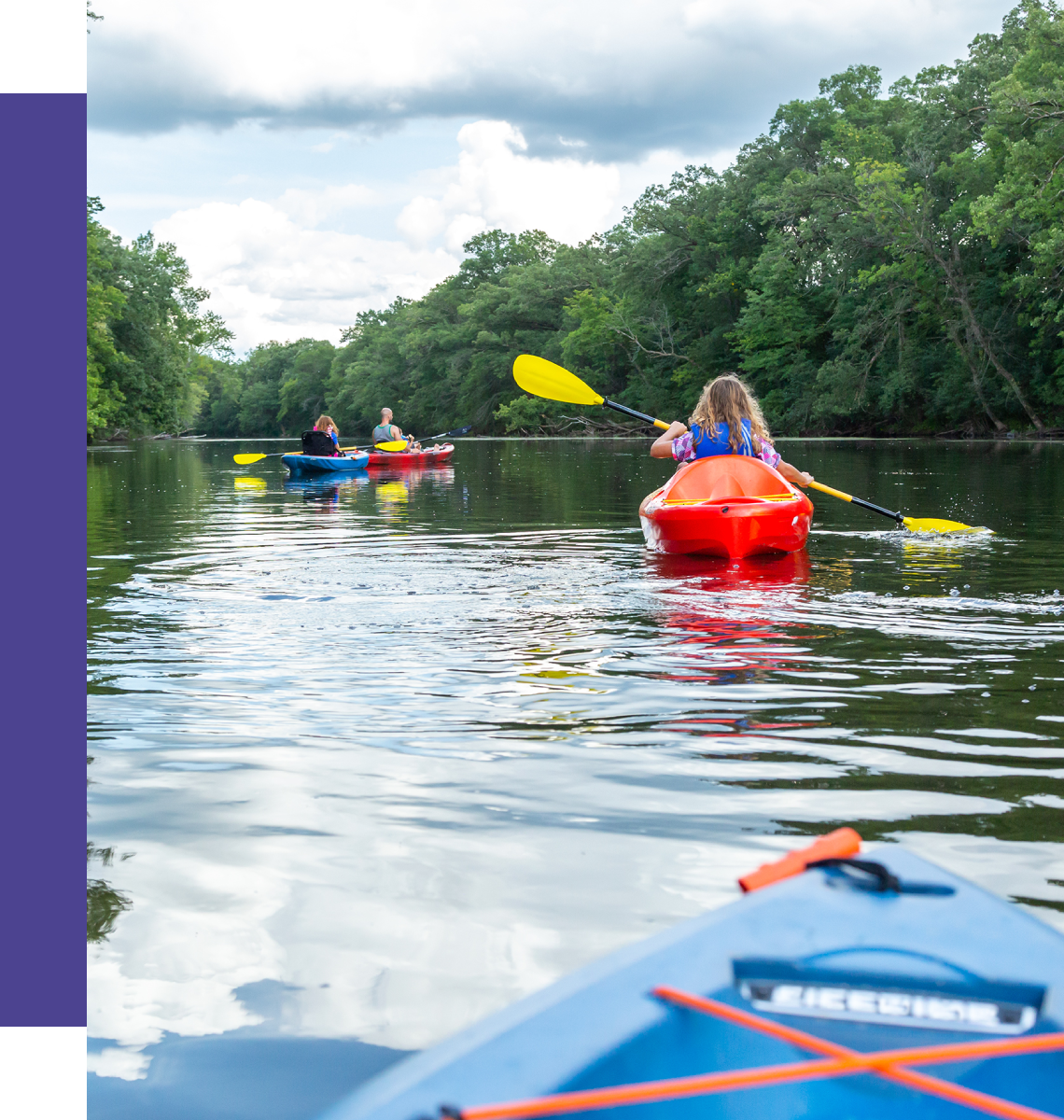 People kayaking on calm river with trees