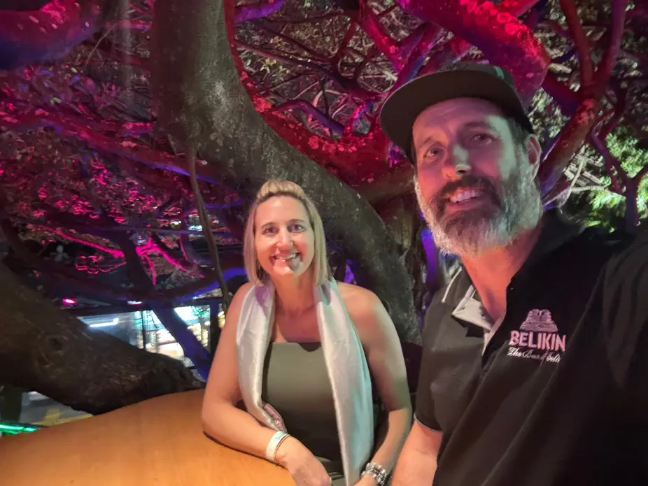 Two people smiling under colorful illuminated tree