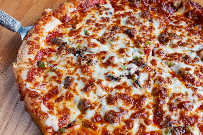 Cheesy pepperoni and sausage pizza on wooden paddle